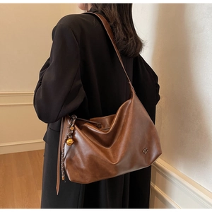 Detail of a large brown leather tote bag with a golden sphere charm on a model's shoulder