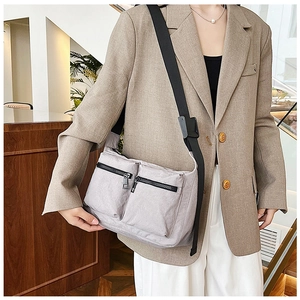 Detail of grey nylon crossbody bag featuring dual front zipper pockets and wide strap