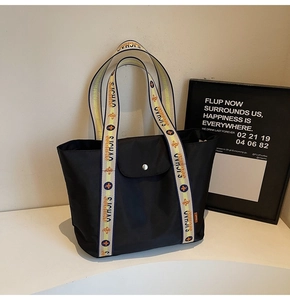 Detail of black tote bag featuring patterned handles with floral and letter prints