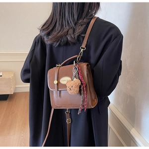 Détail du sac bandoulière marron avec pendentif ours en peluche et sangle tissée