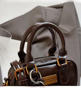 Detail of dark brown glossy handbag showing golden hardware and handle textures
