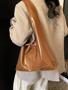 Glossy brown caramel tote bag with decorative knot detail shown as a shoulder bag