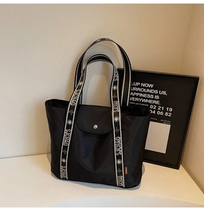 Close-up of black nylon tote bag with silver snap button and branded strap detail