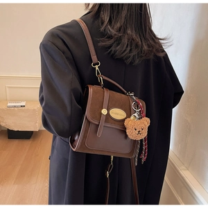 Détail d'un sac à bandoulière marron en patchwork avec cuir mat et breloque d'ours