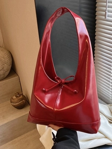Glossy red hobo tote bag with a decorative bow shown in a natural light setting