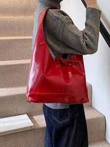 Glossy red faux leather tote bag with side drawstring knot detail shown as an underarm bag