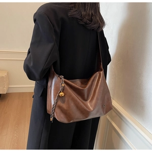 Detail of a brown leather tote bag with woven strap and decorative golden bell charm