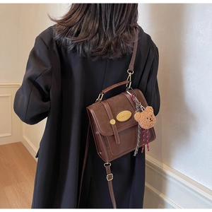 Gros plan d'un sac bandoulière rétro marron en cuir mat avec un joli petit ours suspendu