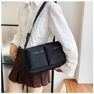 Detail view of black nylon crossbody bag with dual front utility pockets on a model