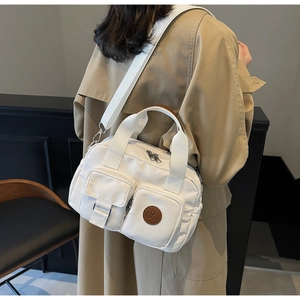 Detailed view of white multi-pocket nylon bag featuring a round cherry logo and wide strap