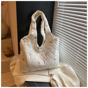 Detail of white quilted tote bag featuring pink bear embroidery and metal button closure