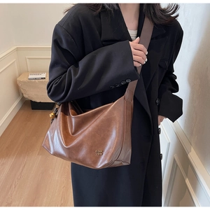 Brown faux leather tote bag with vintage texture and metal logo detail on black blazer