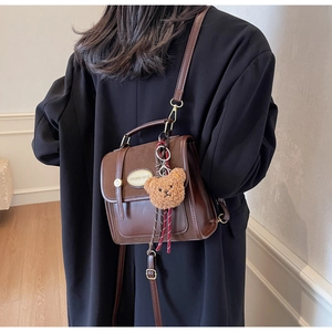 Détail d'un sac à dos en cuir et daim marron foncé avec pendentif ours en peluche