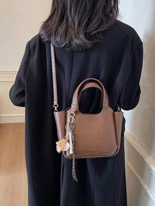 Sac seau vintage marron avec breloque baseball porté par un mannequin en blazer noir