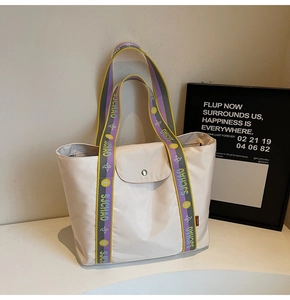 Detail of beige tote bag featuring a colorful woven shoulder strap and magnetic closure