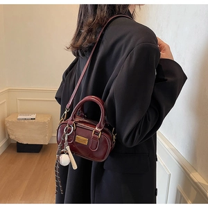 Detail of burgundy leather Boston bag with gold hardware and baseball charm on black blazer
