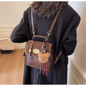 Detail of brown vintage crossbody bag with mixed leather texture and plush bear charm
