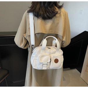 Detail of white nylon handbag featuring dual front pockets and round leather logo patch