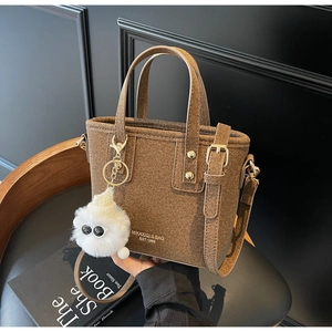 Close-up of brown textured bucket bag with fluffy monster charm and shoulder strap