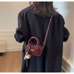 Detail of burgundy glossy mini pillow bag with baseball charms and golden hardware