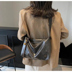 Detail of a large black slouchy hobo bag featuring a decorative golden bell charm on the side