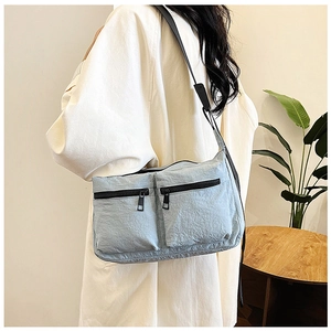 Detail of light blue nylon crossbody bag with dual zip pockets shown on model