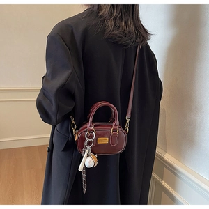 Detail of burgundy mini pillow bag with metallic logo and baseball charm accessory