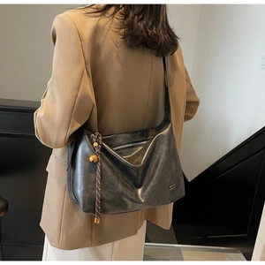 Detail of a black leather tote with gold clock pendant on a model in a beige blazer