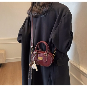 Detail of burgundy PU leather boston bag with baseball charm and golden nameplate