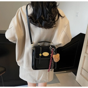 Détail arrière d'un sac bandoulière noir rétro avec breloque ours et foulard à carreaux