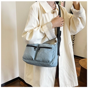 Detail of light blue nylon crossbody bag with black zippers shown on person