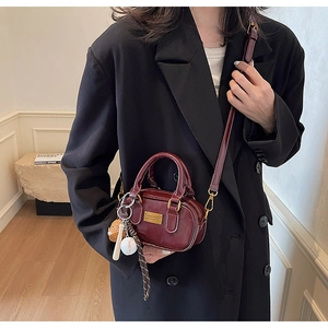 Detail of burgundy glossy mini pillow bag with golden plaque and baseball pendant
