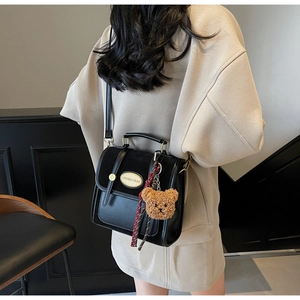 Detail of black retro leather handbag featuring gold metal plate and brown plush bear charm