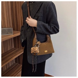 Close-up of brown suede bag with gold hardware and leopard faux fur pom pom charm