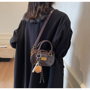Model wearing a dark brown glossy patent leather mini bag with golden hardware and charms