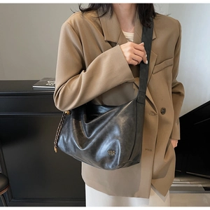 Detail of black leather hobo tote with metallic logo and woven side buckle decoration