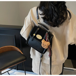 Detail of black leather satchel bag with gold logo and cute brown teddy bear keychain