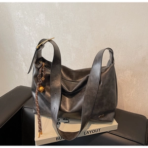 Detail of dark retro leather tote with metallic logo and decorative woven strap