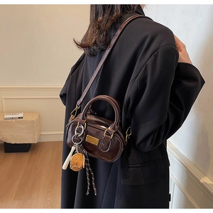Detail view of a dark brown glossy leather Boston bag worn on the shoulder by a model