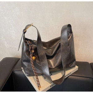 Detail of grey leather tote bag featuring golden hardware and woven bell charm