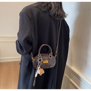 Detail of a dark brown mini pillow bag with gold hardware and a cute charm accessory