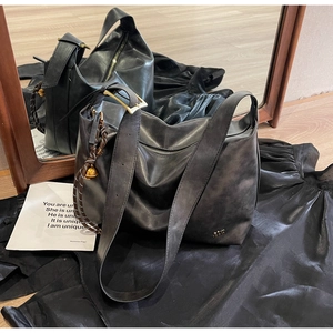 Detail of a large leather tote bag featuring a gold buckle and woven charm on black fabric