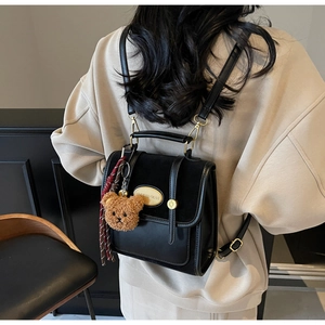 Detail of black faux leather backpack with suede flap and cute teddy bear charm accessory