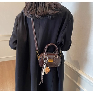 Detailed shot of dark brown mini boston bag with baseball charm and gold logo plate