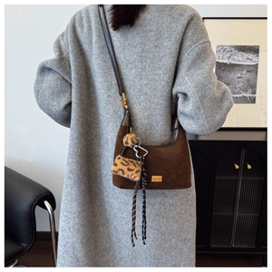 Detail of dark brown suede crossbody bag with leopard plush charm and woven strap accents