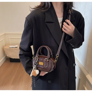 Detail of dark brown glossy patent leather mini Boston bag with baseball pendant