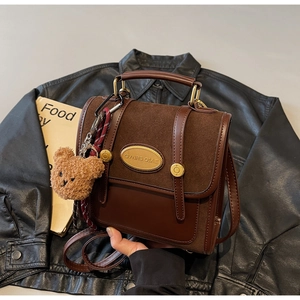 Detail of vintage brown leather backpack with gold metal plate and plush bear charm