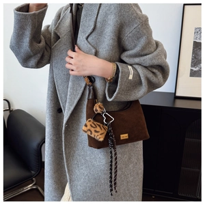 Detail of brown suede shoulder bag featuring Miss mat logo and leopard plush charm