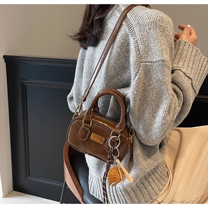 Detail of brown glossy mini handbag with baseball charm and metallic hardware on a model