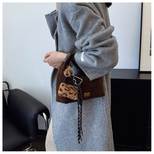 Close-up of brown suede dumpling bag with leopard print pom-pom and braided cord detail